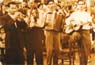 Σχολικές επιδείξεις στην προκυμαία Πλωμαρίου Λέσβου, τη δεκαετία του 1950. Διακρίνονται οι μουσικοί από αριστερά προς τα δεξιά: Γιάννης Παντελέλης (τρομπόνι), Μιχάλης Βερβέρης ή «Τουρκογιάννης» (βιολί), Μανόλης Γιαγνίσης (ακορντεόν), Ηλίας Ρουμελιώτης ή «Καραχάλιας» (κιθάρα).